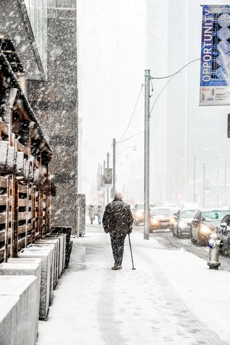 A person walking with a cane along a snow-covered sidewalk.
